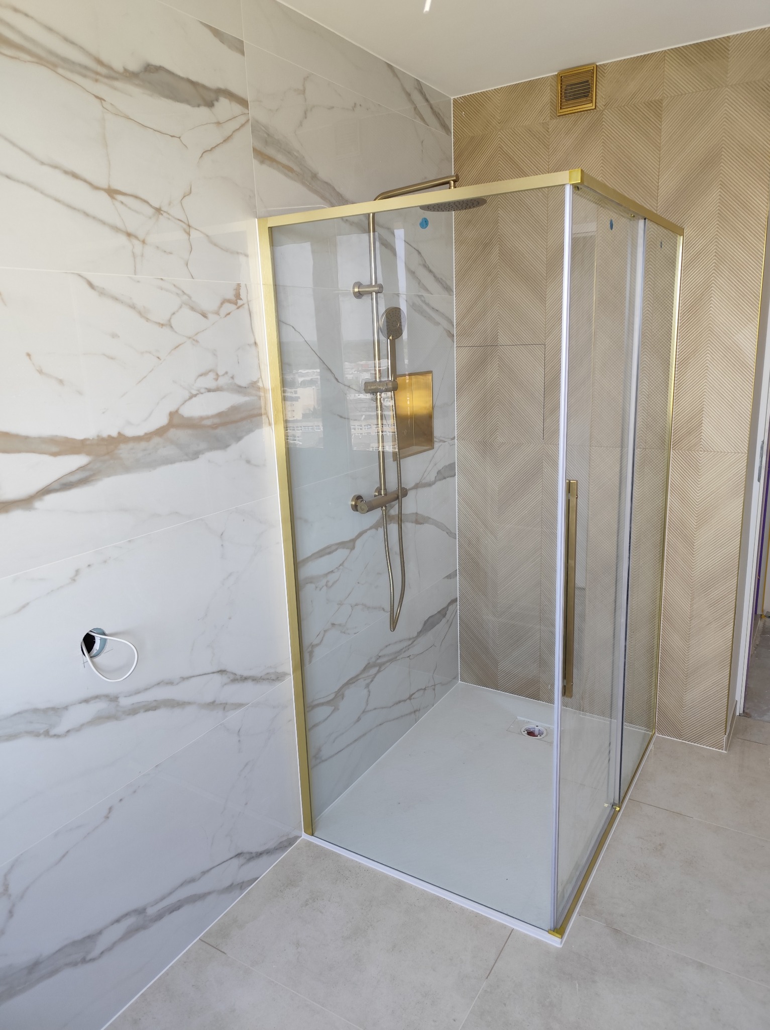 Nowoczesna kabina prysznicowa z złotymi profilami, marmurowe i geometryczne płytki ścienne, jasna podłoga. Minimalistyczny design łazienki po remoncie.