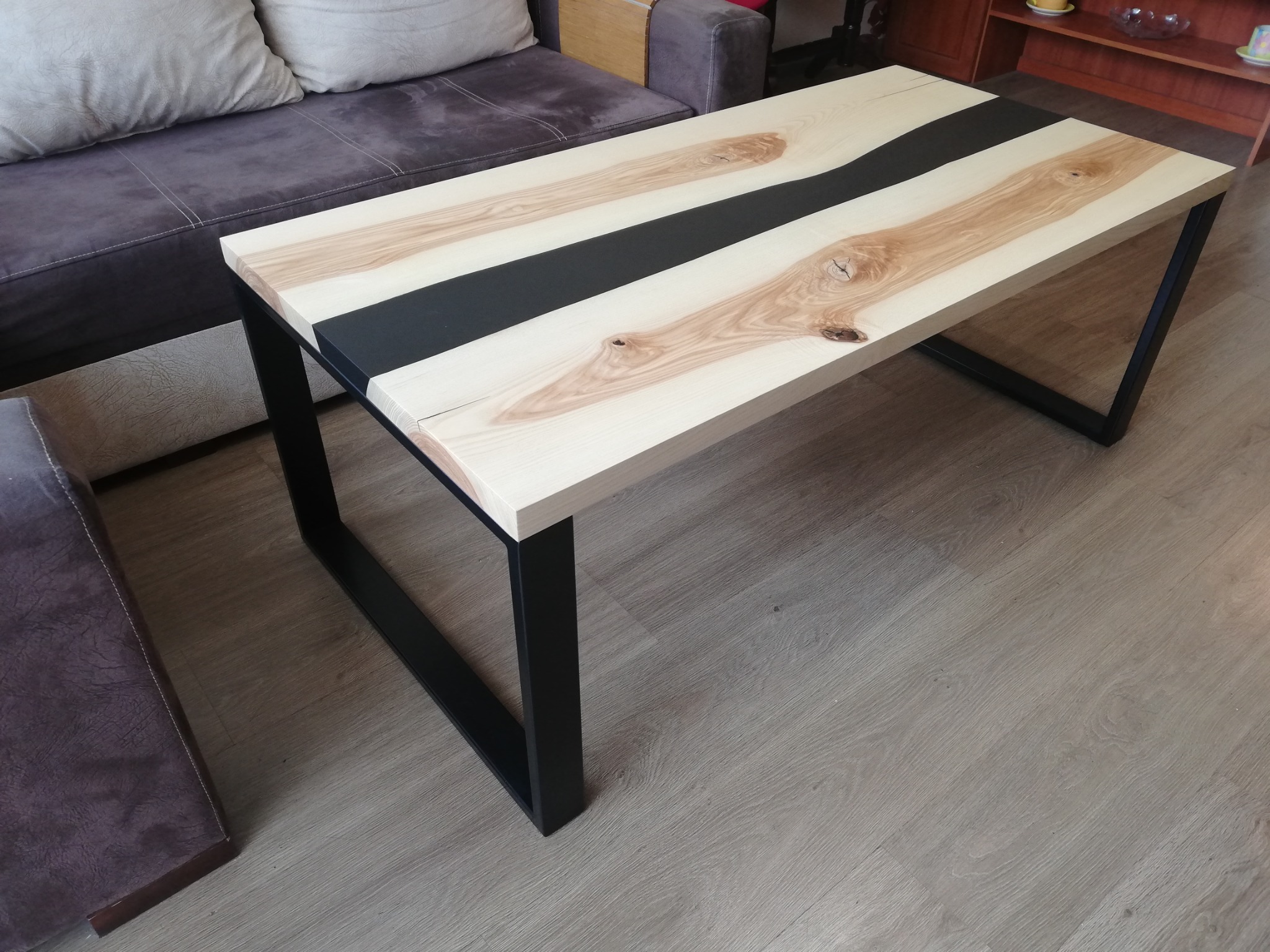 Stolik z blatem z drewna Jesionu i czarnej żywicy w środkowej czesci. Nogi ze stali malowane proszkowo.