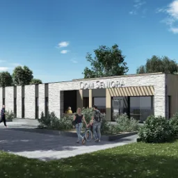 Wizualizacja budynku Domu Seniora z elewacją z jasnej cegły i drewnianymi panelami, otoczonego zielenią i spacerującymi osobami w słoneczny dzień.