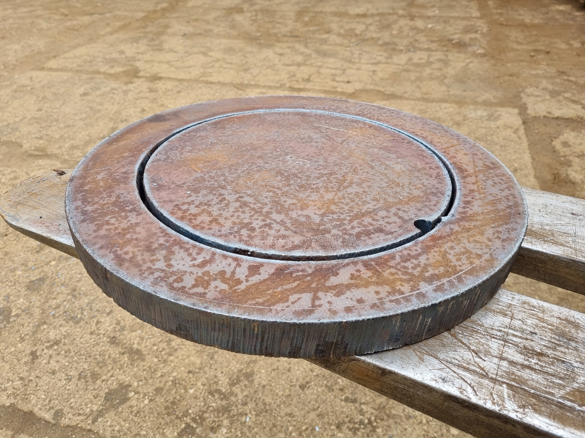 Okrągły, metalowy element z wyżłobieniem, leżący na drewnianym stole, widoczne ślady rdzy i obróbki metalu.