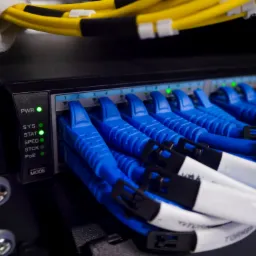 Panel krosowniczy z podłączonymi niebieskimi kablami sieciowymi i żółtymi kablami w górnej części, diody LED sygnalizujące status połączenia, widoczne śruby mocujące.