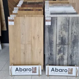 Ekspozycja próbek paneli podłogowych marki Abaro w różnych odcieniach: jasny dąb Carmel i szary Siena, z widocznym logo producenta.