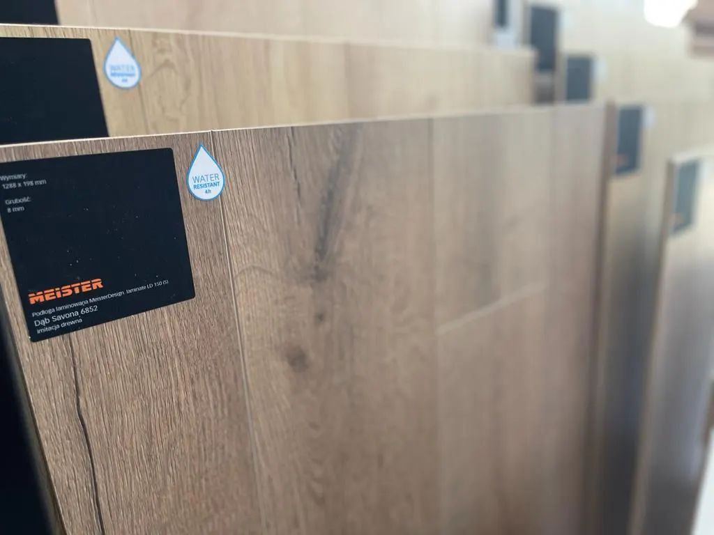 Próbki paneli laminowanych Dąb Savona 6852, z etykietami informacyjnymi o wymiarach i odporności na wodę, prezentowane w pionie.