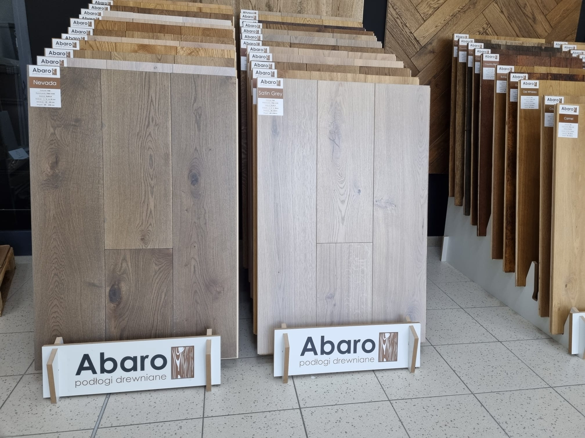 Ekspozycja paneli podłogowych marki Abaro w odcieniach Nevada i Satin Grey, prezentowanych na stojakach z logo firmy.