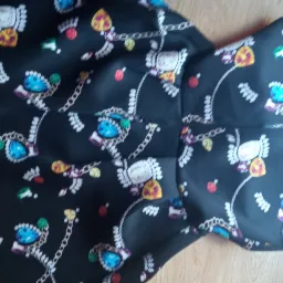 Fragment czarnej sukienki z wzorem łańcuchów i klejnotów, leżącej na drewnianej podłodze w Nowych Skalmierzycach.