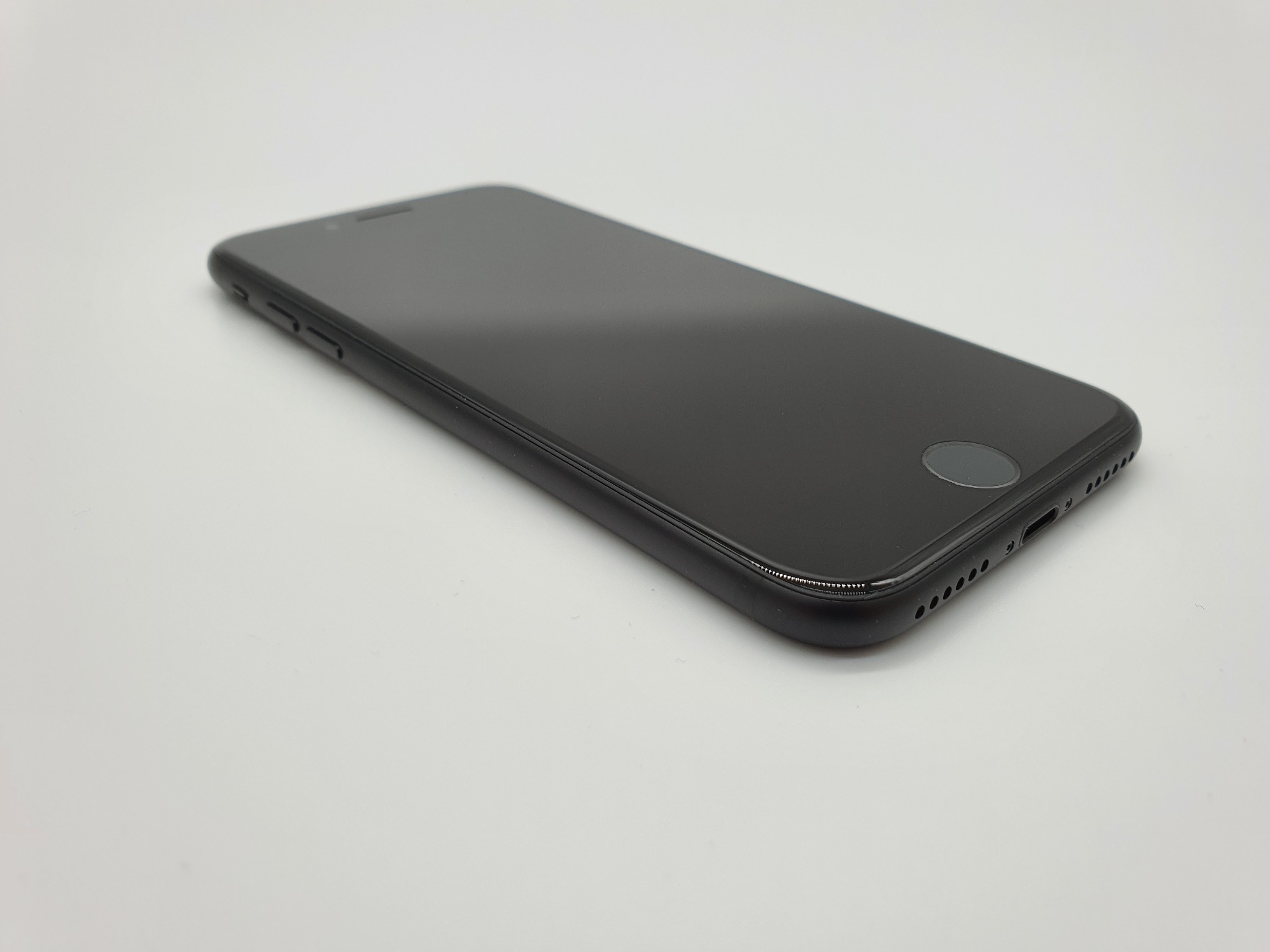 Czarny smartfon leżący na białym tle, widoczny z boku, ekran wyłączony, ukazujący głośniki i przyciski boczne.