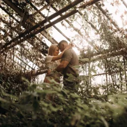 Para obejmująca się w szklarni z roślinnością, ciepłe światło słoneczne przebija przez konstrukcję dachu.