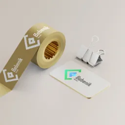 Wizualizacja identyfikacji marki: wizytówka z zaokrąglonymi rogami i rolka taśmy z powtórzonym logo, obok metalowy klips biurowy na jasnym tle.