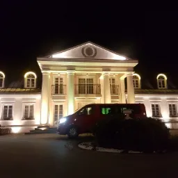 Czerwony van na tle podświetlonego, klasycystycznego budynku z kolumnami, nocne ujęcie.