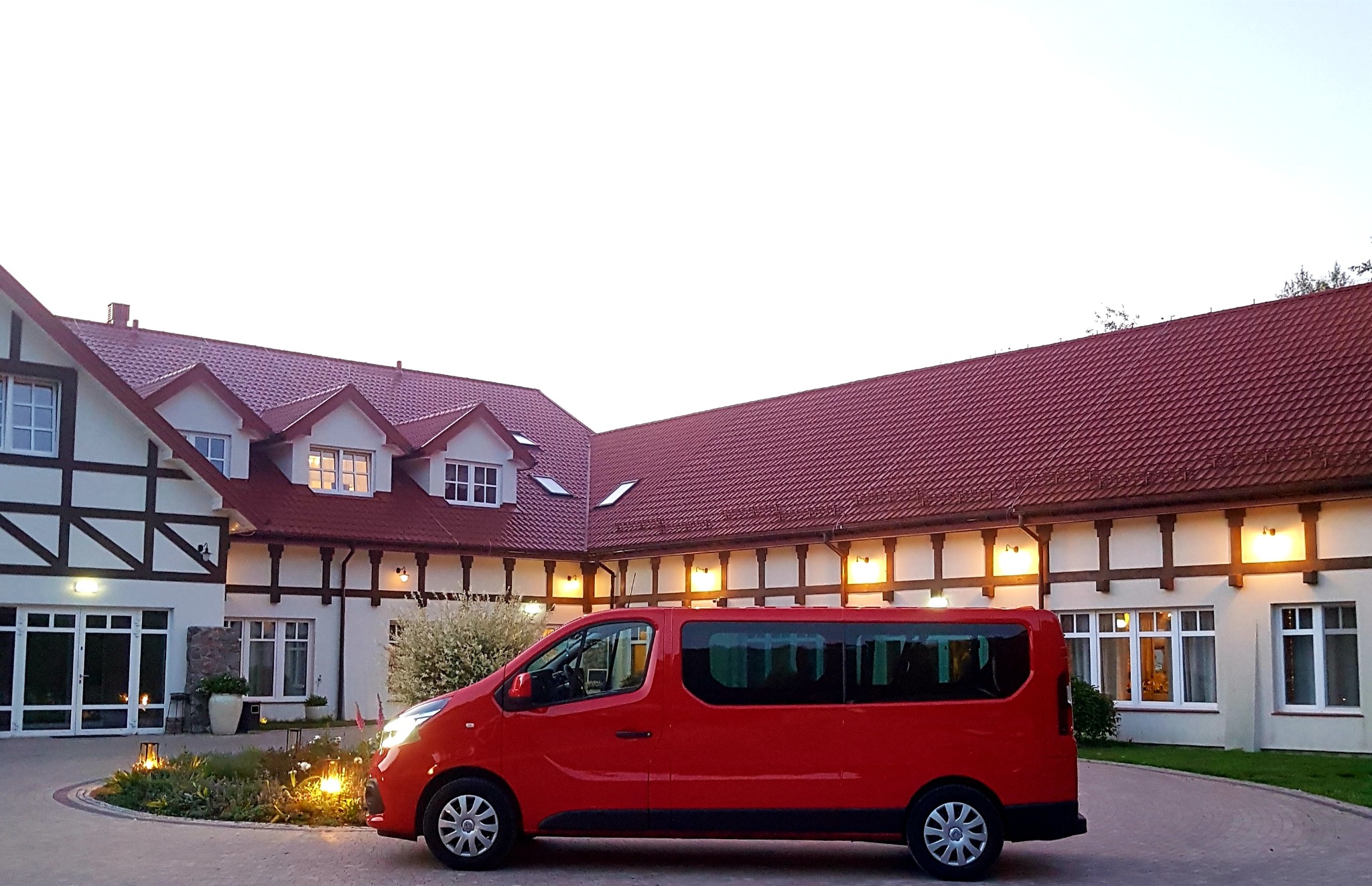 Czerwony bus przed budynkiem w stylu rustykalnym z czerwonym dachem i białymi ścianami z drewnianymi elementami dekoracyjnymi.