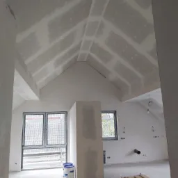 Poddasze w trakcie wykańczania: zamontowane płyty kartonowo-gipsowe na skosach sufitu, widoczne łączenia wymagające szpachlowania, okna dachowe, przygotowane punkty instalacji elektrycznej...