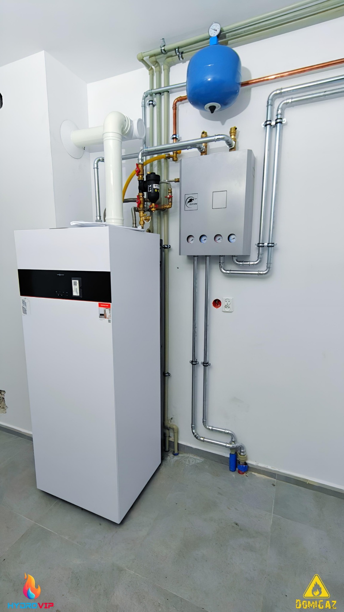 Nowoczesny, biały piec grzewczy z podłączonymi rurami miedzianymi i stalowymi, zbiornik wyrównawczy w kolorze niebieskim, szara szafka sterownicza z manometrami zamontowana na ścianie, widoczne...