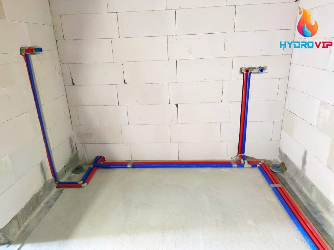 Nowa instalacja wodna z rur PEX, kolory niebieski i czerwony, prowadzone po ścianach z białego betonu komórkowego i wylewce podłogowej, widoczne złącza i logo firmy w prawym górnym rogu.