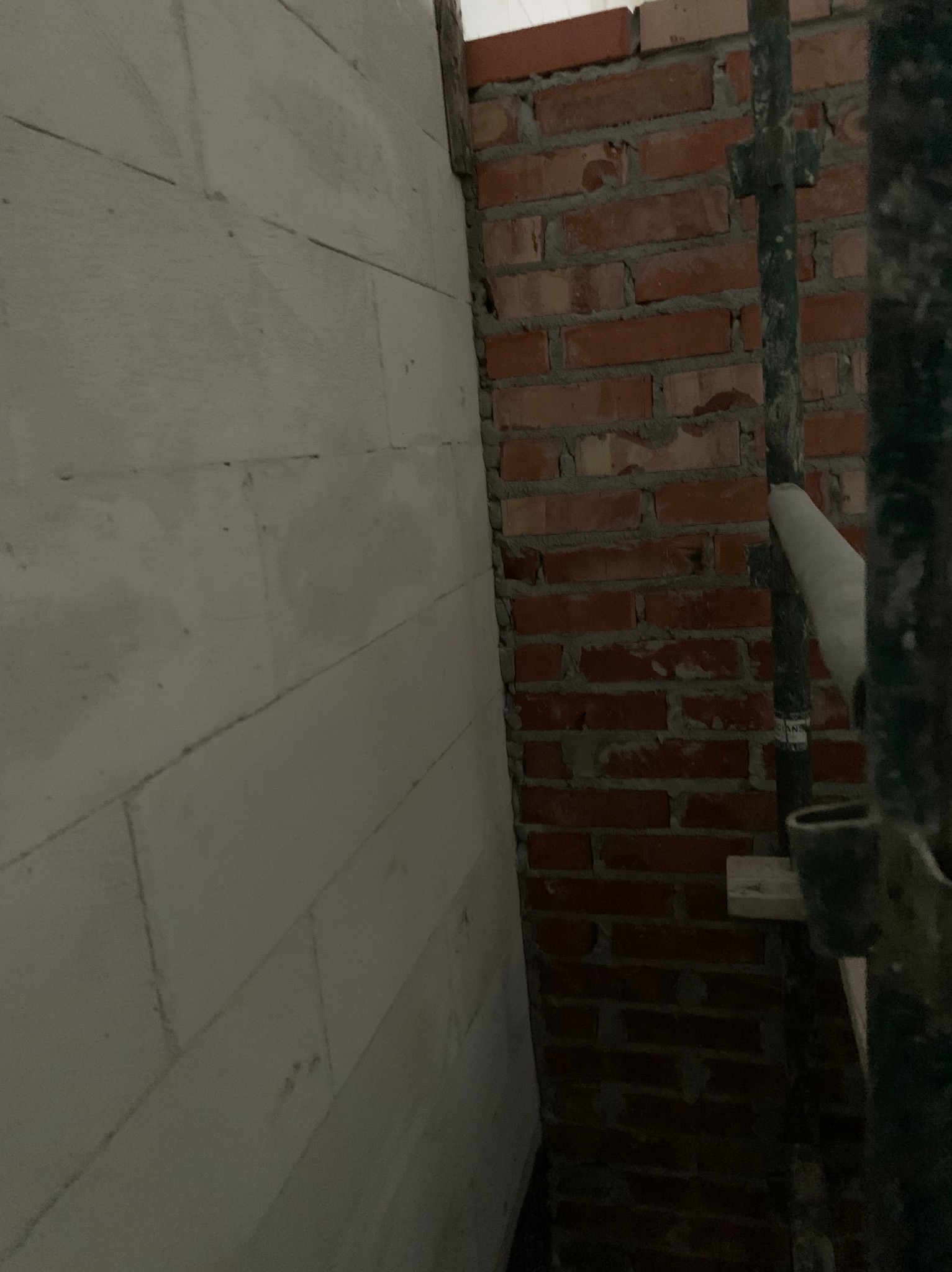 Wnętrze w trakcie budowy: ściana z białych bloczków obok ściany z czerwonej cegły. Fragment rusztowania po prawej stronie. Widok z bliska na surowe materiały budowlane.