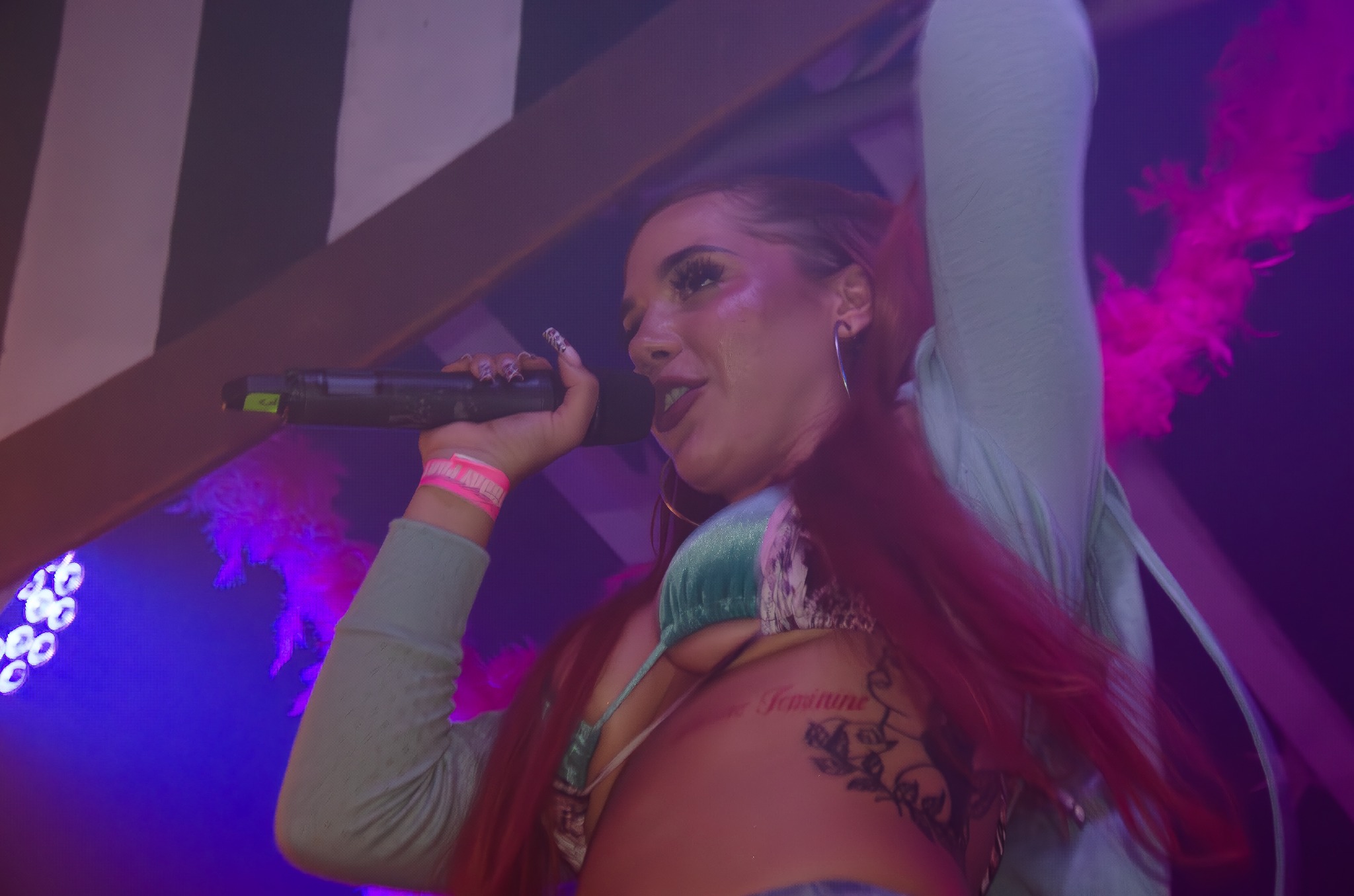 Koncertowe ujęcie w fioletach: wokalistka z tatuażem, mikrofon w dłoni, energia sceniczna i dynamiczne światła tworzą unikalny, artystyczny klimat.