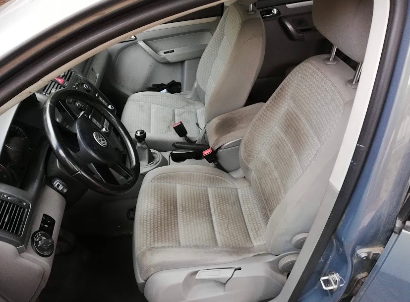 Wnętrze samochodu z widocznymi, wyraźnie zabrudzonymi jasnymi fotelami przednimi, wymagającymi prania tapicerki.