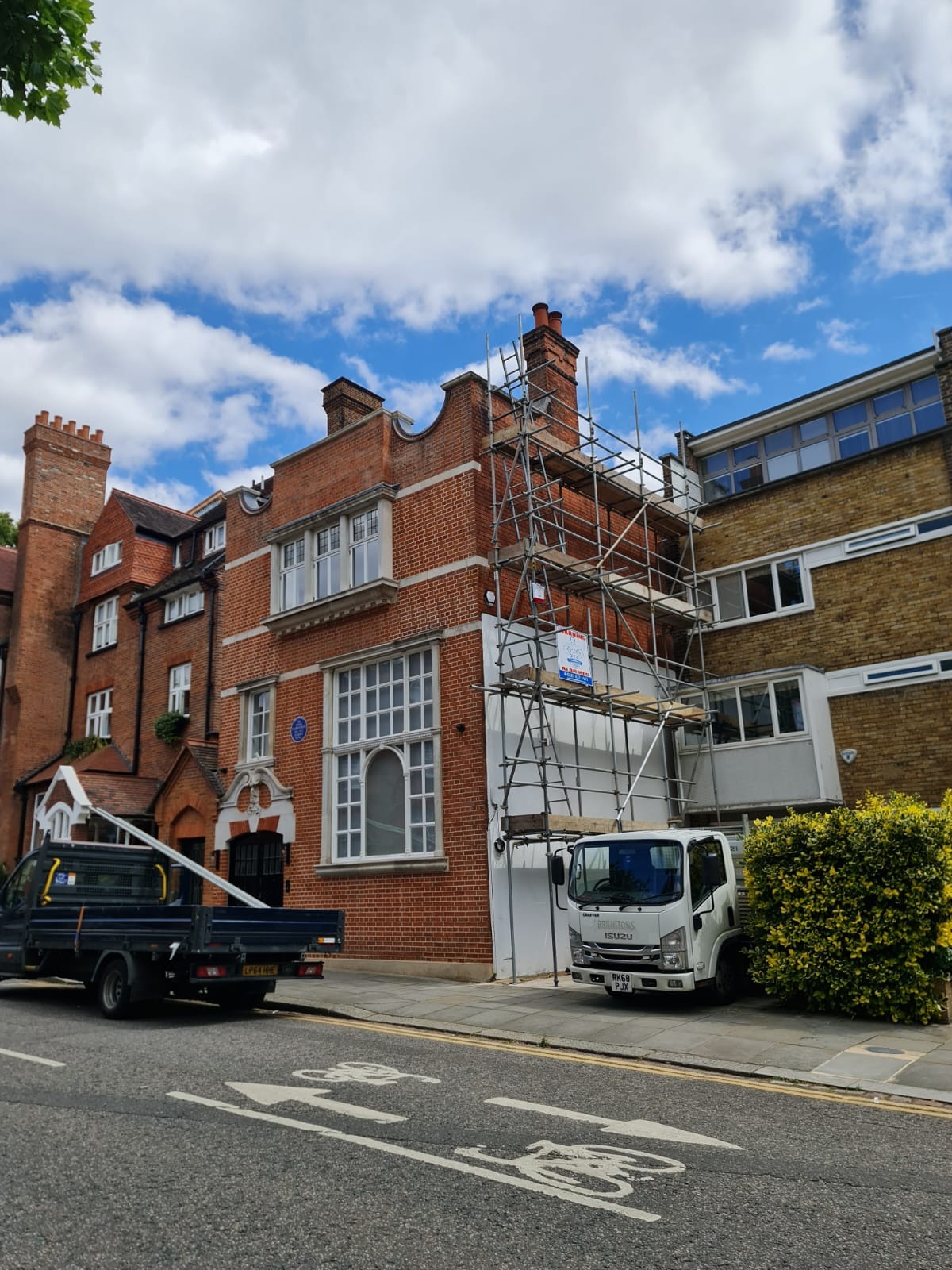 Budynek z cegły z rusztowaniem i zaparkowanym samochodem dostawczym, widok z ulicy.