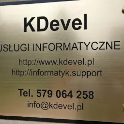 Tabliczka informacyjna firmy KDevel z Lublina, oferującej usługi informatyczne, z adresem strony internetowej i numerem telefonu, zamocowana na złotych śrubach.