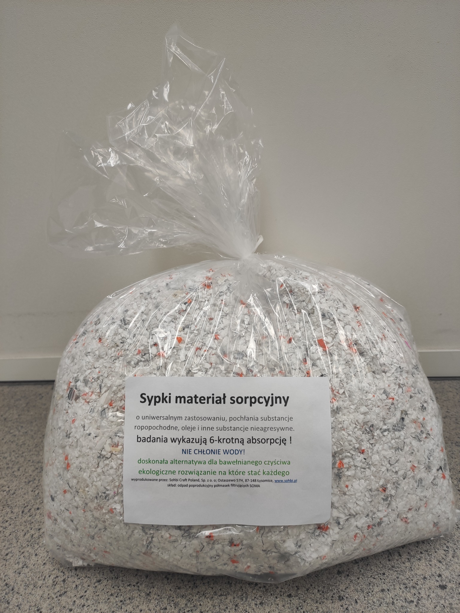 Worek foliowy wypełniony sypkim materiałem sorpcyjnym z fragmentami pomarańczowych elementów, przeznaczonym do pochłaniania substancji ropopochodnych i olejów, z etykietą informacyjną na froncie.