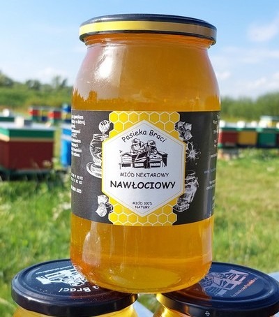 Słoik miodu nektarowego nawłociowego z etykietą Pasieka Braci, w tle ulice z ulami.