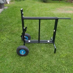 Czarny, spawany wózek transportowy z dużymi kołami o niebieskich felgach, stojący na trawniku.