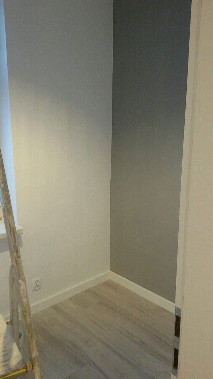 Pomieszczenie po remoncie: ściany pomalowane na biało i szaro, podłoga wyłożona panelami imitującymi drewno, widoczna drabina malarska przy oknie.