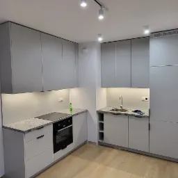 Jasnoszara, nowoczesna kuchnia z granitowymi blatami, oświetleniem punktowym i drewnianą podłogą.