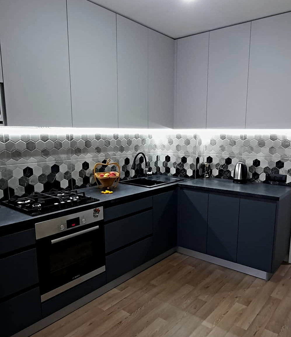 Nowoczesna kuchnia w Warszawie z szarymi szafkami górnymi i granatowymi dolnymi, heksagonalne płytki na ścianie i drewniana podłoga, oświetlenie LED pod szafkami.