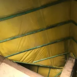 Poddasze z widoczną żółtą folią izolacyjną między zielonymi belkami konstrukcyjnymi, ujęcie od dołu.