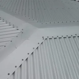 Fragment szarego, blaszanej dachu z widocznymi łączeniami i nitami, sfotografowany pod kątem.