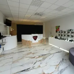 Wnętrze punktu usługowego z ladą recepcyjną z logo 'QFIX Serwis', półkami z laptopami i tabletami oraz ekspozycją smartfonów w gablotach na marmurowej podłodze.