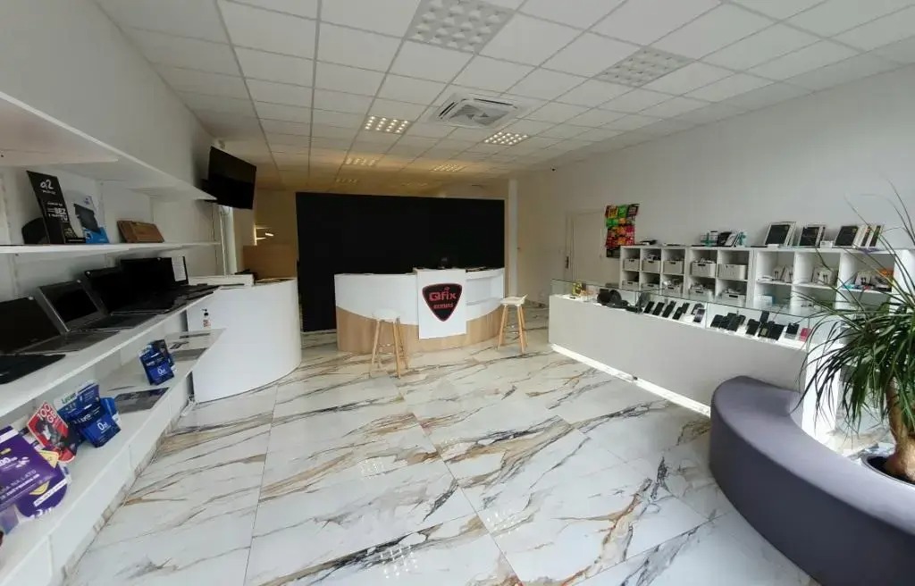 Wnętrze punktu usługowego z ladą recepcyjną z logo 'QFIX Serwis', półkami z laptopami i tabletami oraz ekspozycją smartfonów w gablotach na marmurowej podłodze.