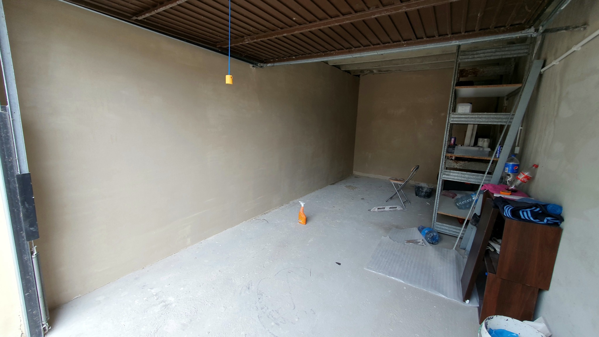 Wnętrze garażu po nałożeniu gładzi szpachlowej na ściany, z widocznymi narzędziami, drabiną i plastikową butelką po środku czyszczącym na podłodze.