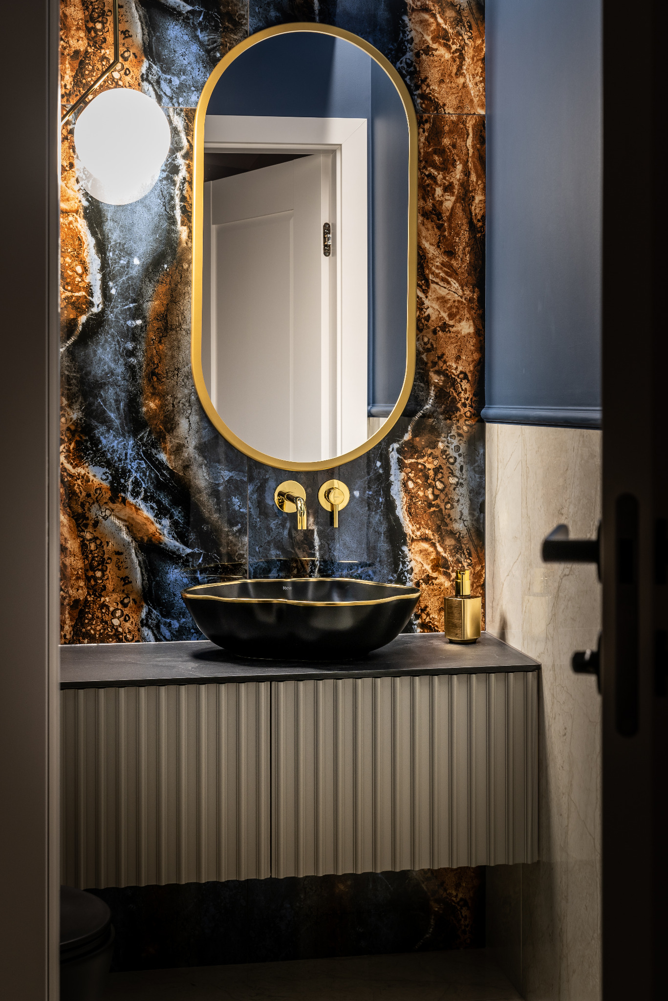 Elegancka łazienka z umywalką nablatową, złotą armaturą i lustrem w złotej ramie na tle ściany z płytek imitujących marmur.