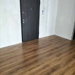 Wnętrze pokoju po położeniu paneli podłogowych w odcieniach brązu, widoczne ślady szpachlowania na ścianach i ciemne drzwi wejściowe.