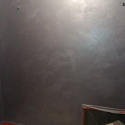 Dat-fix Radosław Data - Ściana pokryta dekoracyjną, szarą powłoką z efektem chmur, zabezpieczona taśmą malarską przy suficie i podłodze, z widoczną drabinką malarską i folią ochronną.