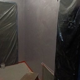 Dat-fix Radosław Data - Świeżo pomalowane ściany w odcieniach szarości z delikatnym efektem dekoracyjnym, zabezpieczone folią meble i schodki malarskie w pomieszczeniu w trakcie prac wykończeniowych.