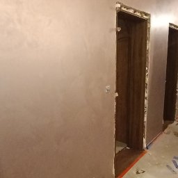 Dat-fix Radosław Data - Wnętrze w trakcie prac wykończeniowych: ściany pokryte gładzią w odcieniach beżu, surowe ościeżnice drzwiowe z widocznymi resztkami pianki montażowej, zabezpieczona podłoga, fragment taśmy...