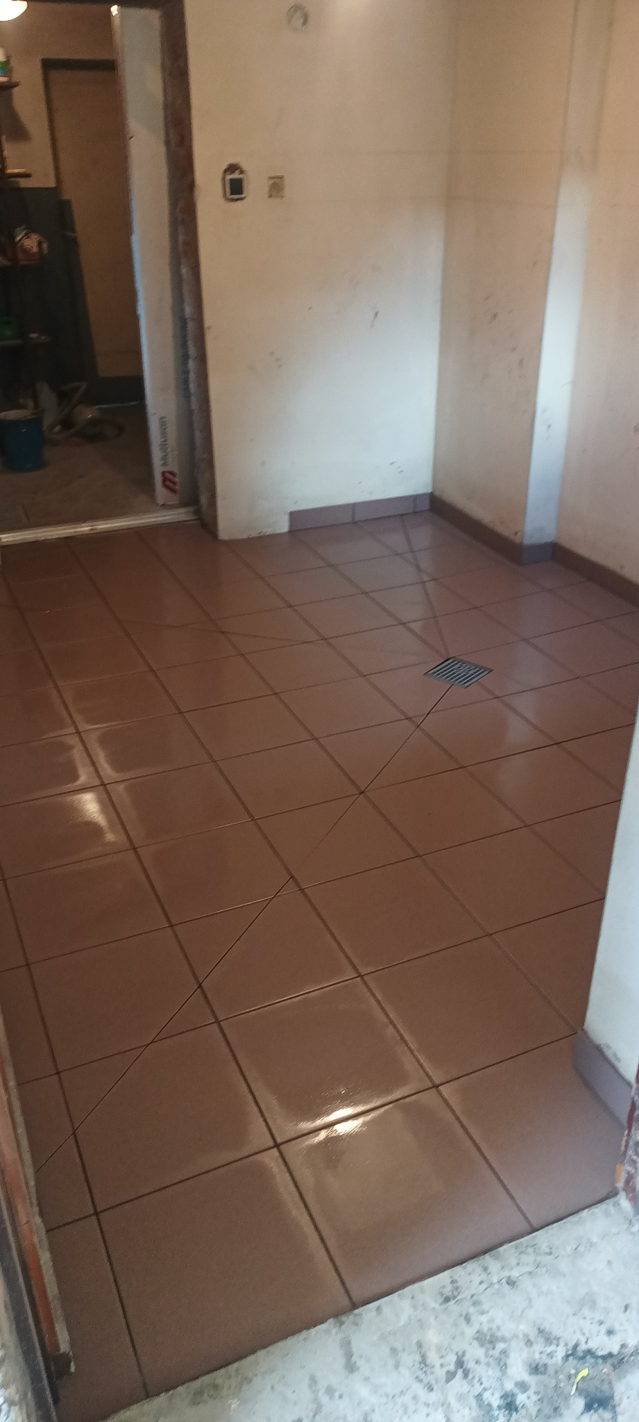 Świeżo ułożone, brązowe płytki podłogowe w łazience z odpływem liniowym, widoczne niedoskonałości na ścianach przed dalszymi pracami wykończeniowymi.