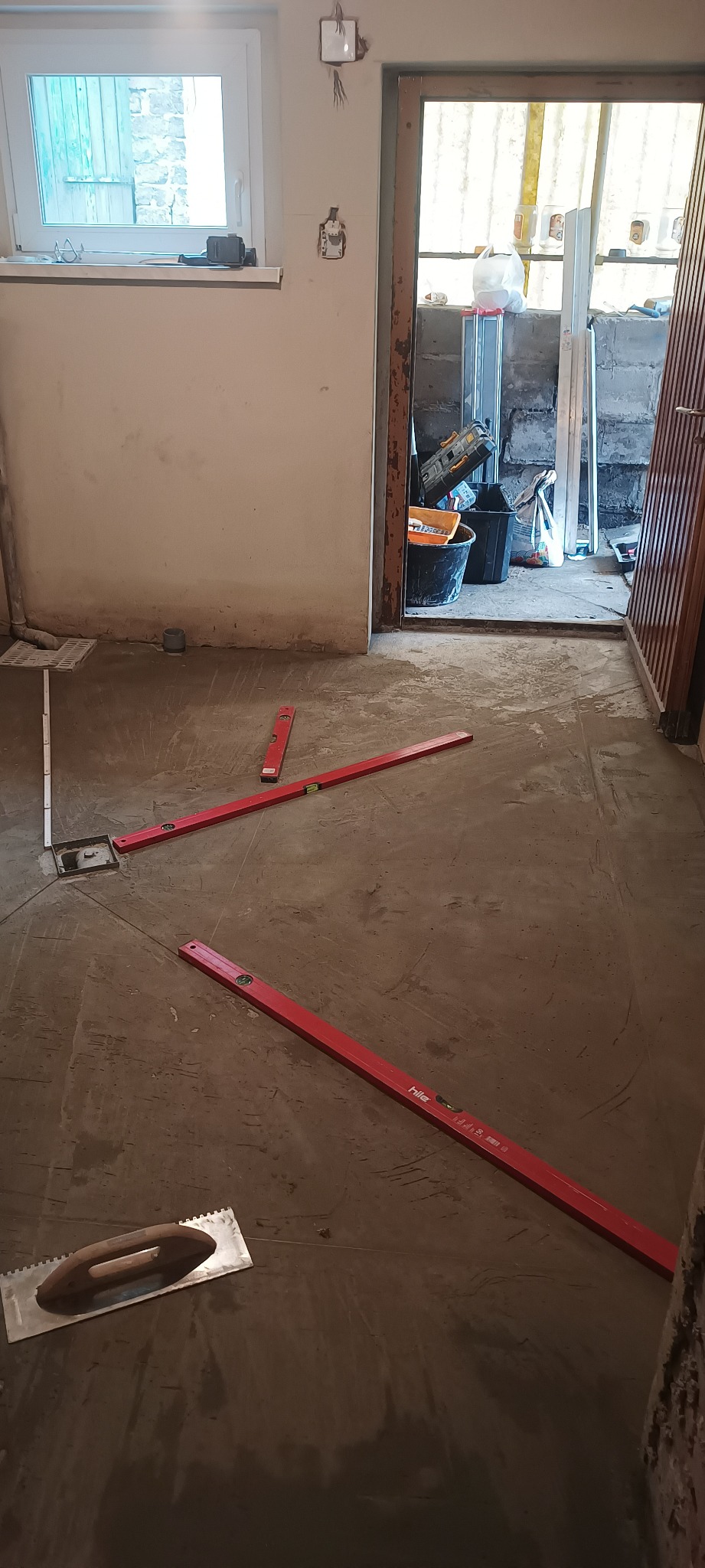 Przygotowanie podłoża pod płytki: wylewka samopoziomująca z użyciem poziomnic laserowych i pacy ząbkowanej, widoczne ślady po wylewce.