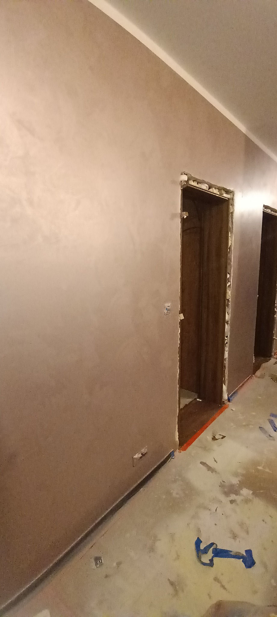 Wnętrze w trakcie prac wykończeniowych: ściany pokryte gładzią w odcieniach beżu, surowe ościeżnice drzwiowe z widocznymi resztkami pianki montażowej, zabezpieczona podłoga, fragment taśmy...