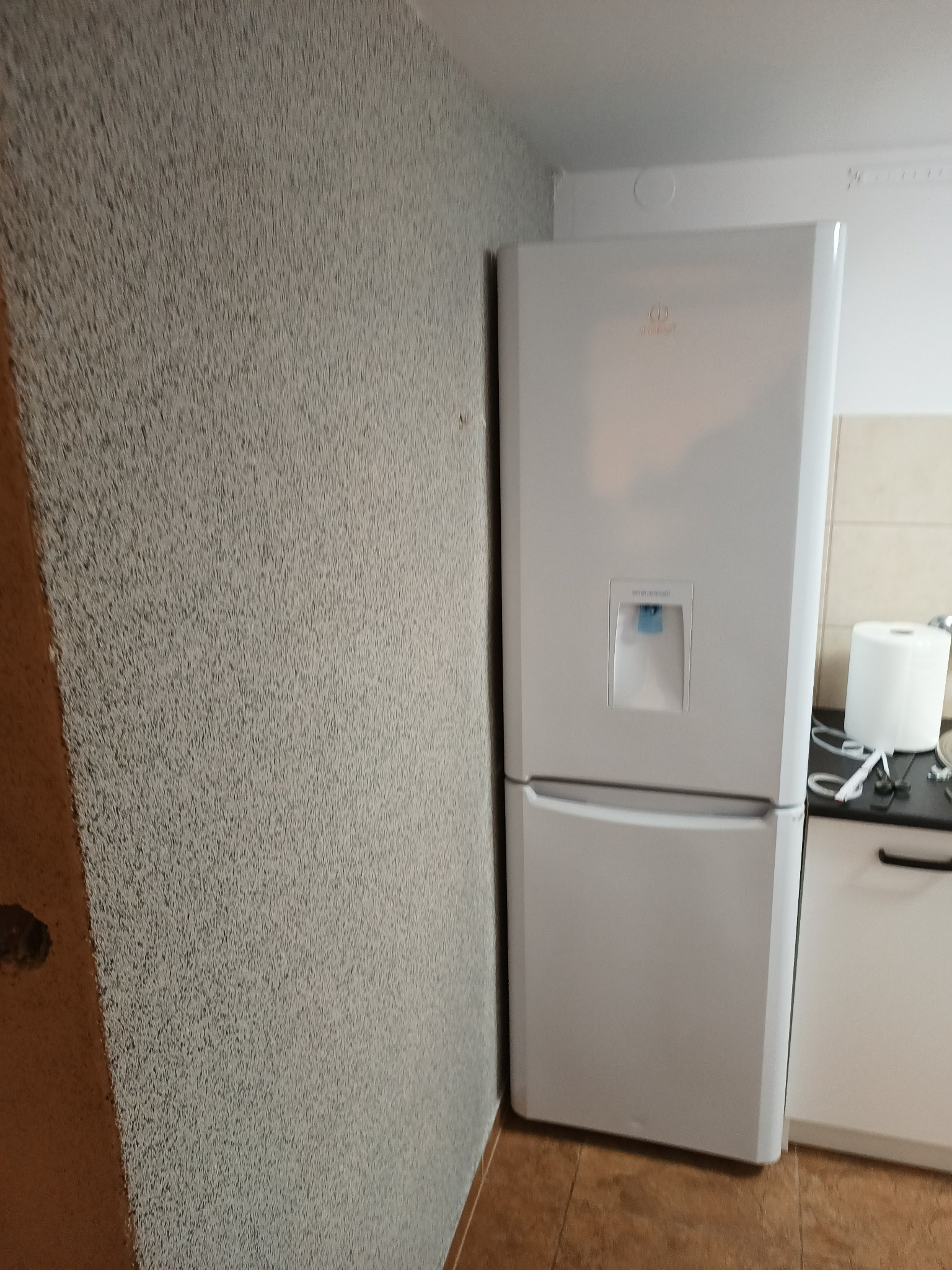 Ściana z efektem baranka w szarym odcieniu, sąsiadująca z białą lodówką w kuchni z jasnymi meblami.