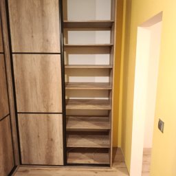 Mebl-Art Meble na Wymiar - Jasna szafa wnękowa z przesuwnymi drzwiami i otwartymi półkami, wykończona w odcieniach drewna, z czarnymi akcentami, w jasnym wnętrzu.