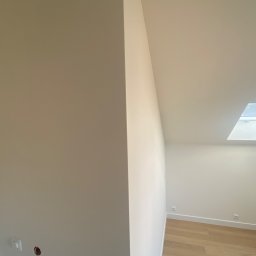 Stanislaw Myroshnychenko - Świeżo pomalowane, jasne wnętrze poddasza z oknem dachowym i drewnianą podłogą, widoczne gniazdka elektryczne i otwór na instalację.