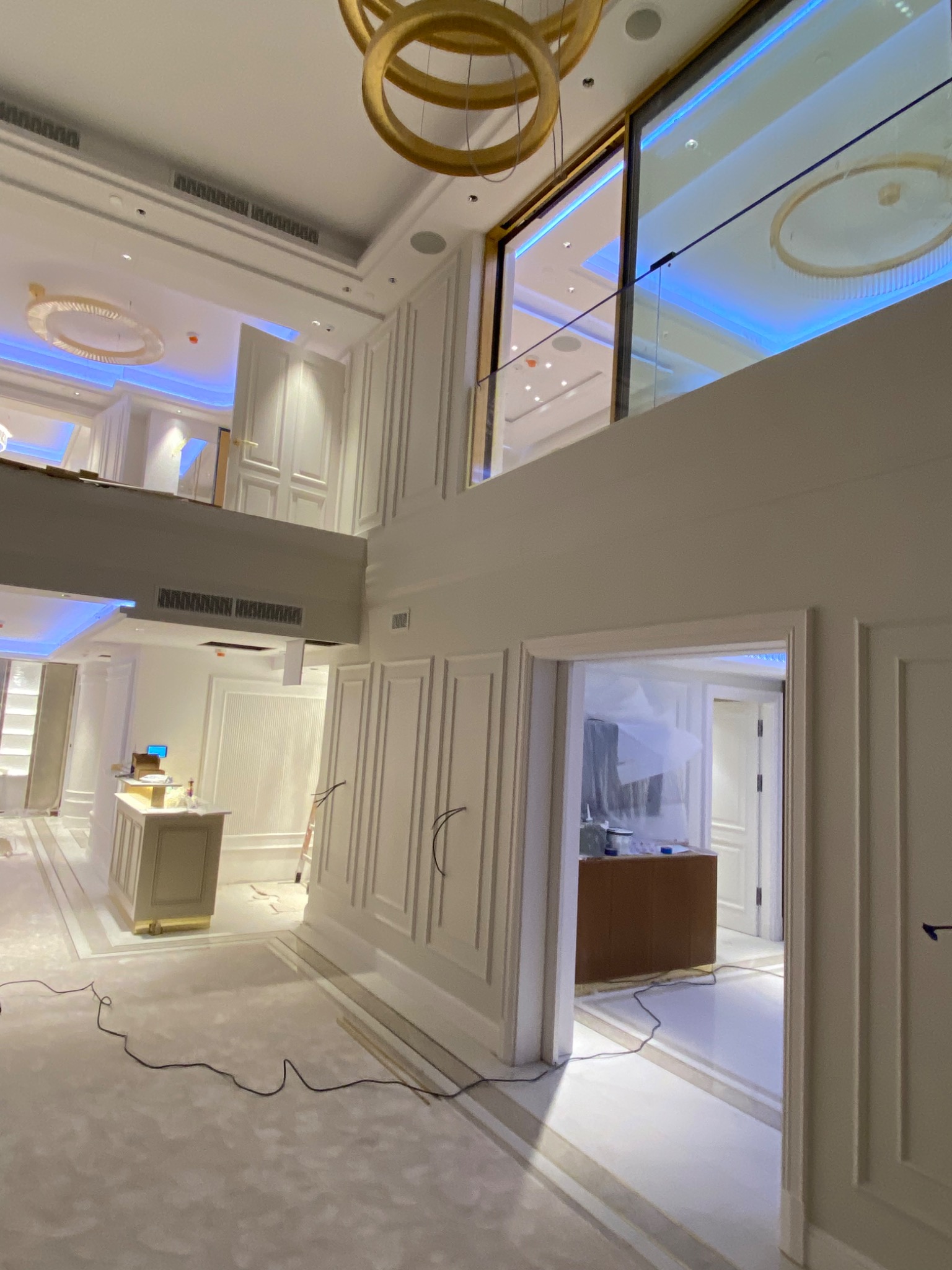 Dwupoziomowe wnętrze w trakcie prac wykończeniowych, widoczne kable na podłodze, zabezpieczone meble i dekoracyjne panele ścienne.