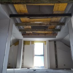 Mat-Bud Bryskiewicz - Montaż sufitu podwieszanego z płyt kartonowo-gipsowych, widoczne drewniane stemple podtrzymujące konstrukcję, pomieszczenie w stanie surowym.