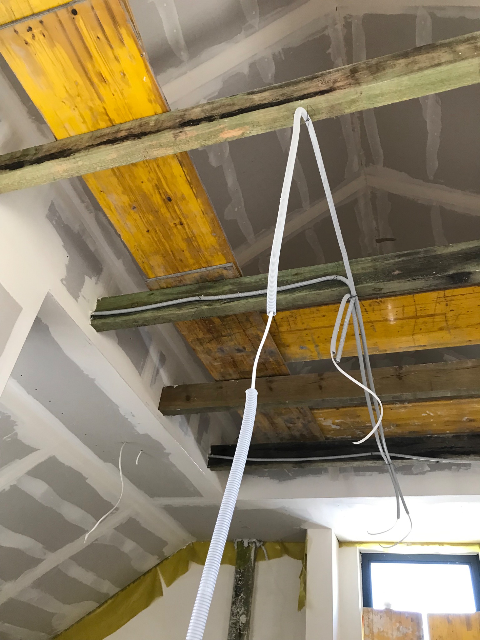 Montaż instalacji elektrycznej w nowo budowanym pomieszczeniu z płyt kartonowo-gipsowych, widoczne kable w peszlach i drewniane elementy konstrukcyjne.