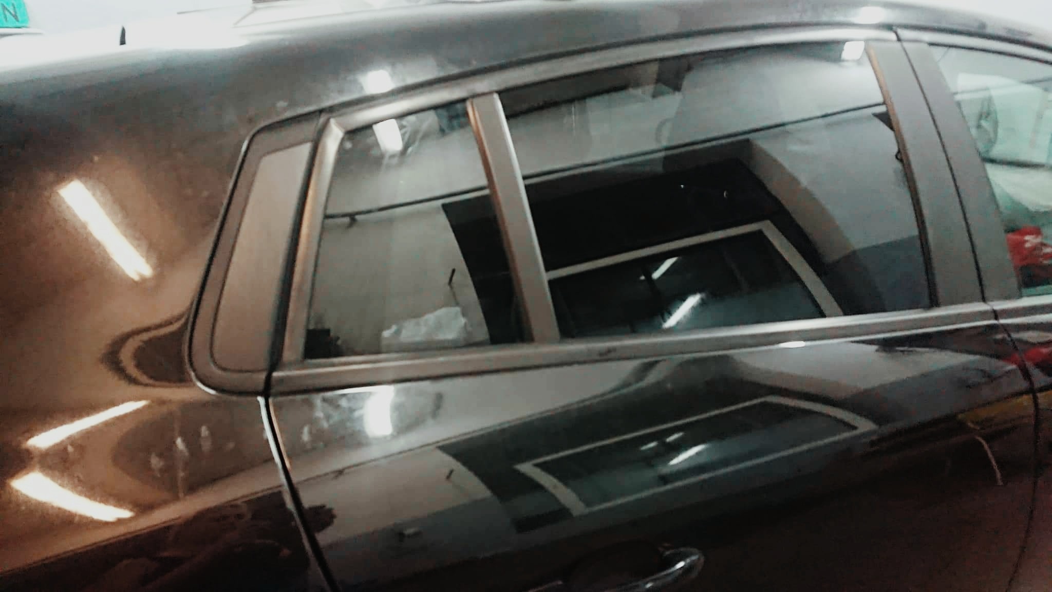 Ciemny samochód z przyciemnionymi szybami bocznymi; widoczne odbicia świateł w karoserii.