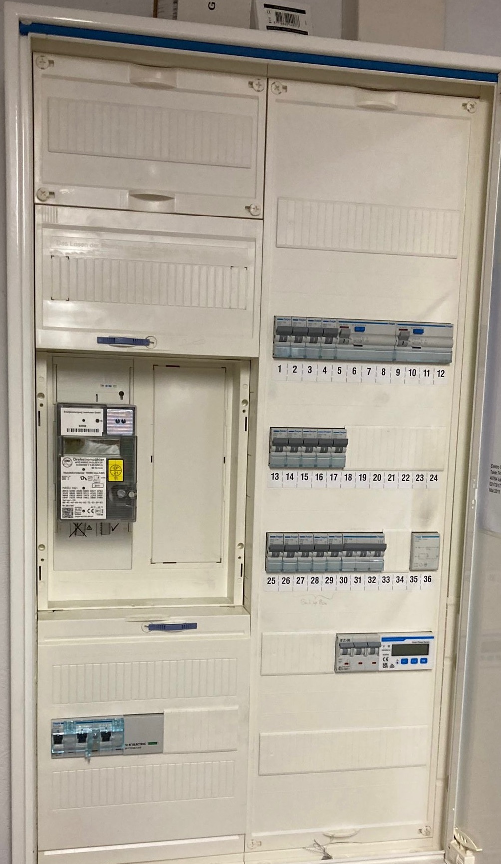 Otwarta skrzynka rozdzielcza z licznikiem energii elektrycznej i bezpiecznikami, widoczne oznaczenia numerów bezpieczników.