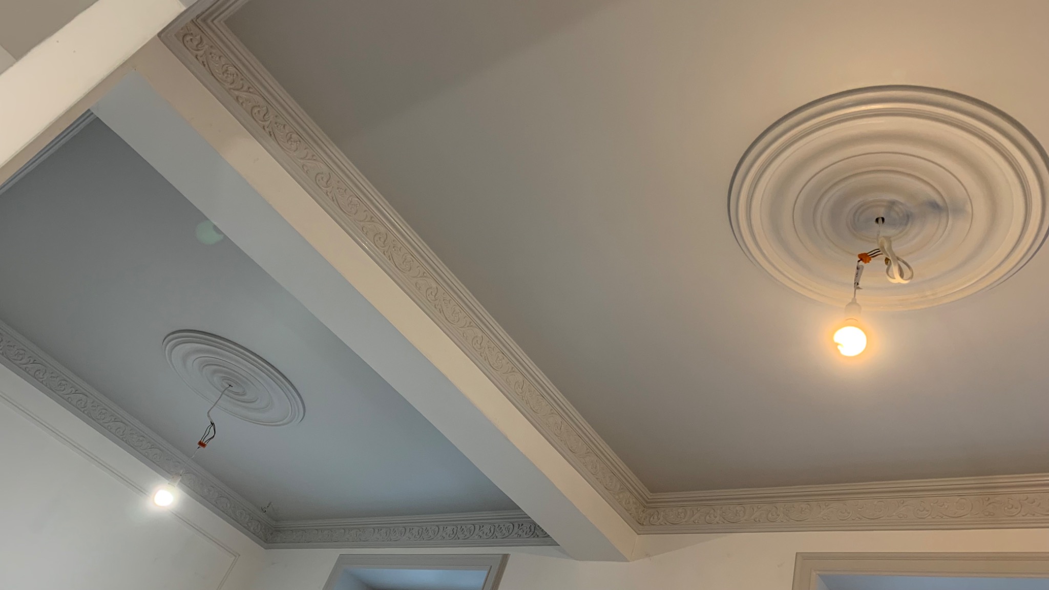 Wykończony sufit z dekoracyjnymi listwami i rozetami, widoczne podłączenia elektryczne do lampy.